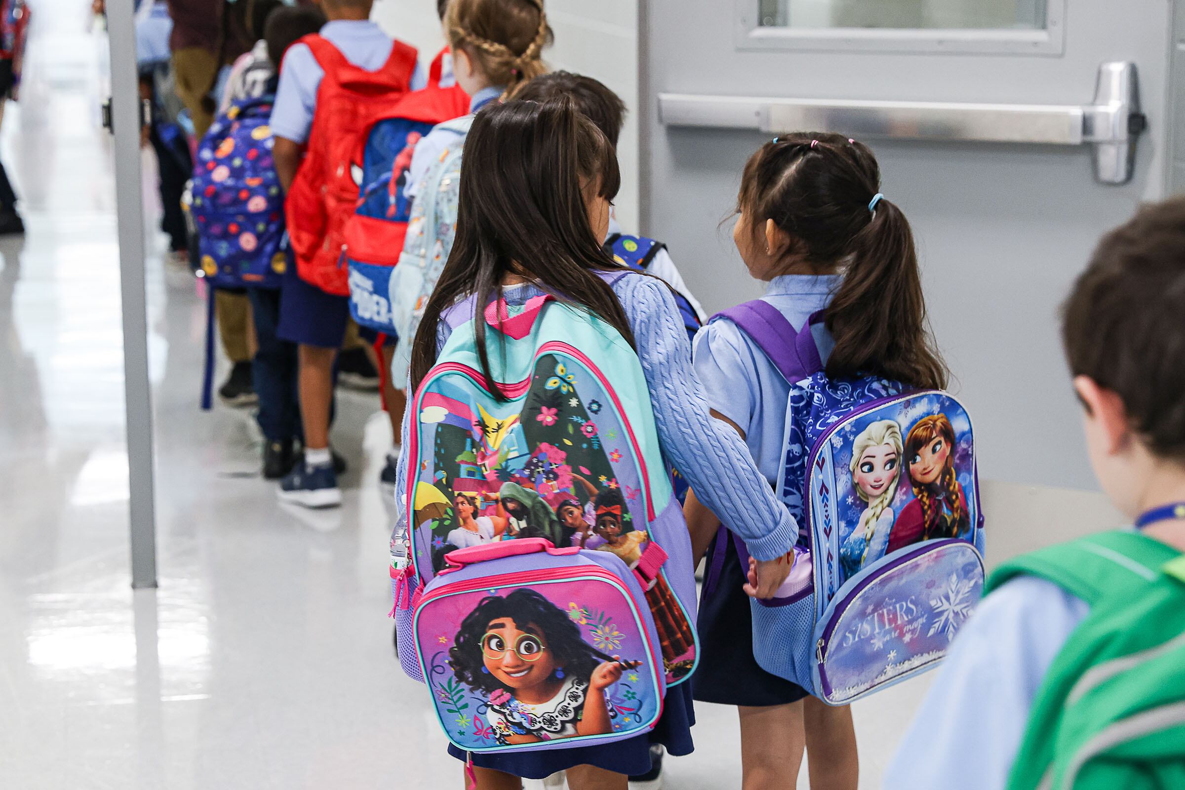 A line of students with backpacks in a school hallway.