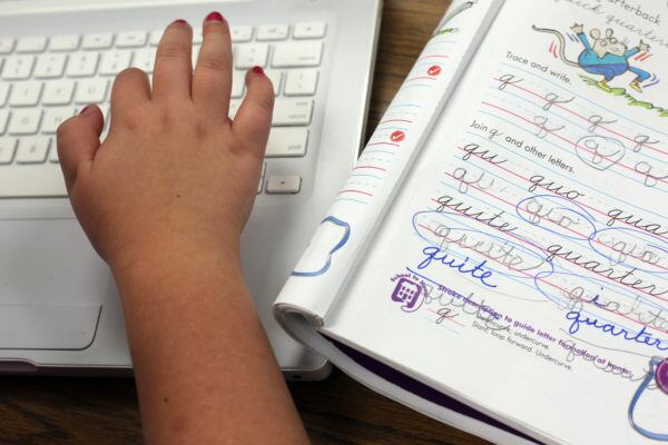 A student types on a laptop after finishing a cursive lesson.