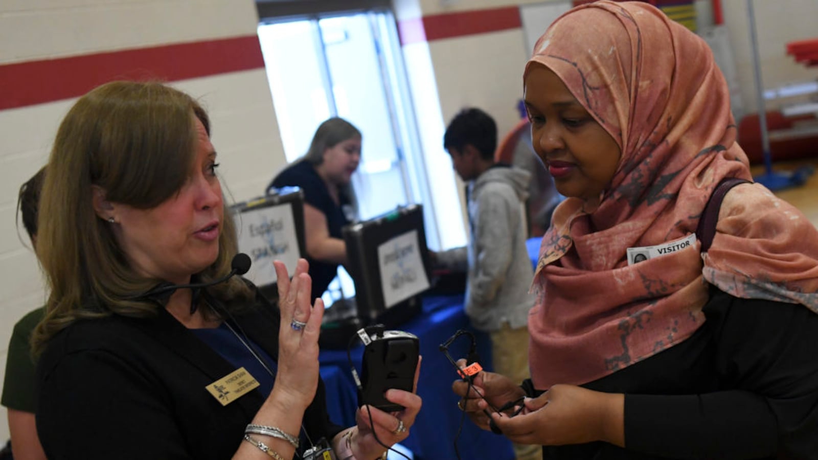 Patricia Shaw, an interpreter for Aurora Public Schools, left, shows Indonesia Maye how to use the transmitters during a back-to-school event at Aurora West College Preparatory Academy on August 6. Maye was hired by the district to interpret to Somali students and their families at the event. (Photo by RJ Sangosti/The Denver Post)