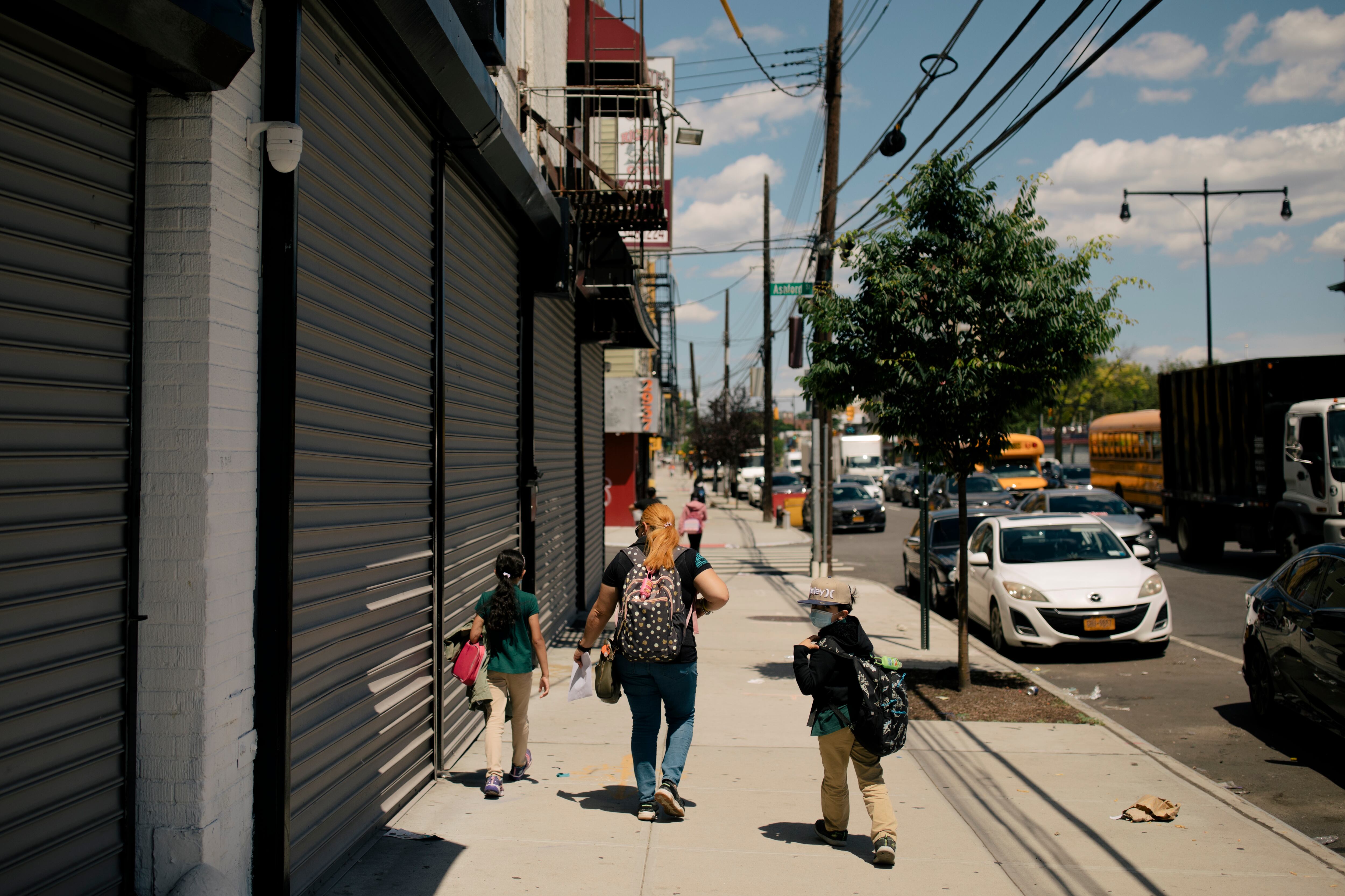 Students walk down the side walk with a tree and cars on the right side.