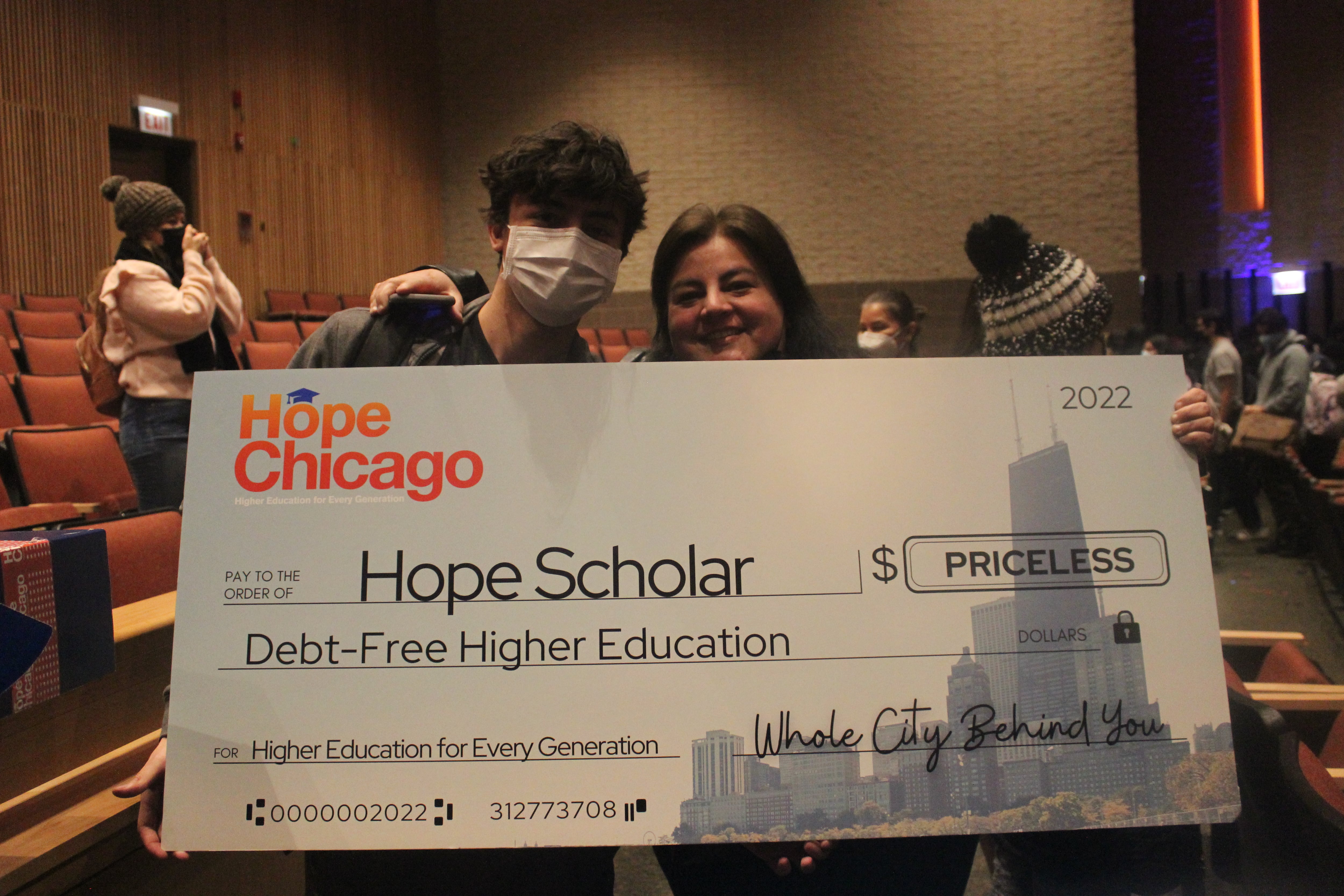 A teenage boy and woman hold a super-sized check for a free college education.