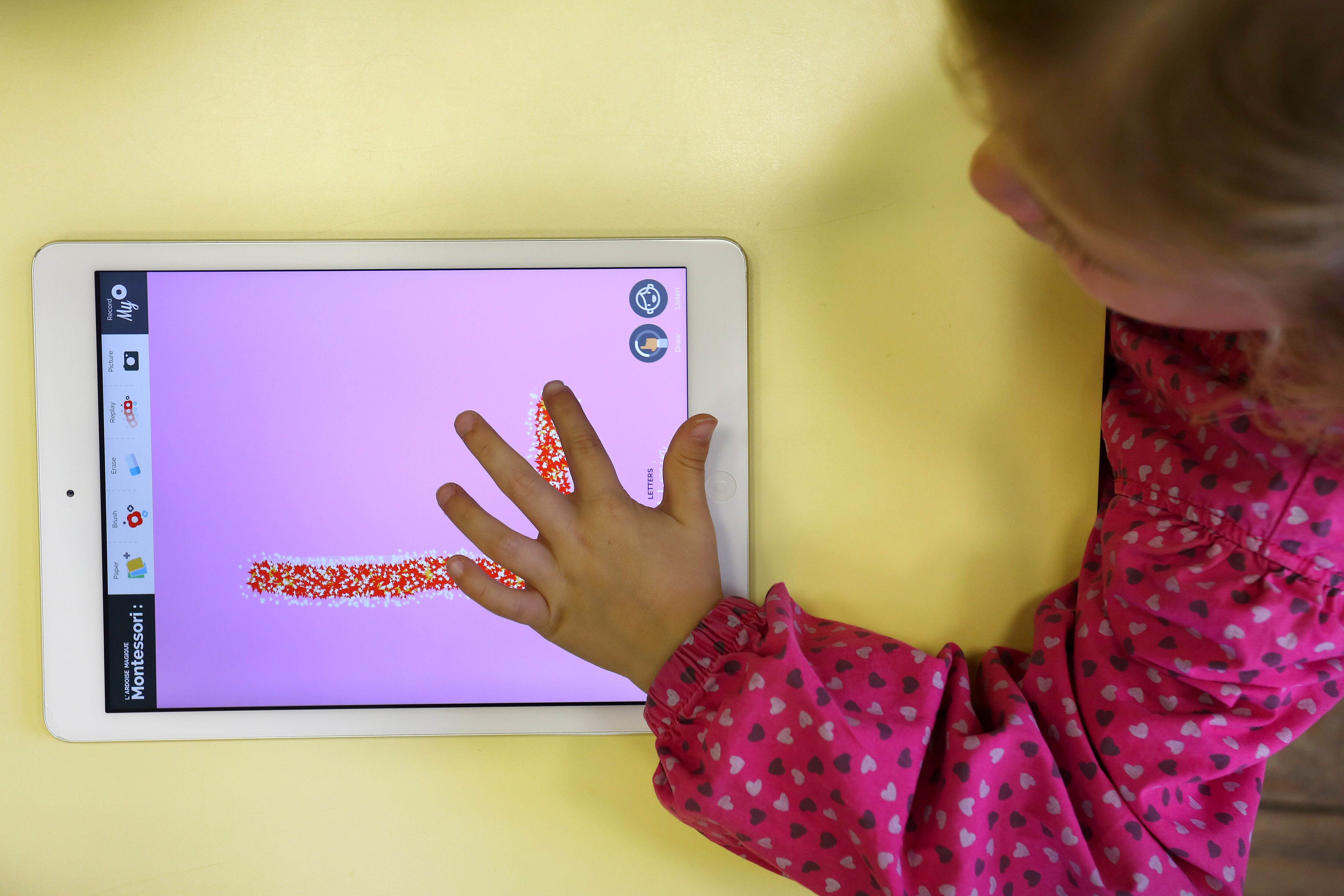 Young girl uses a digital tablet to draw letters (here, an L).