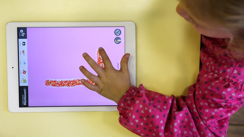 Young girl uses a digital tablet to draw letters (here, an L). 