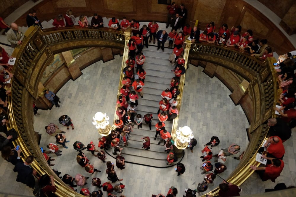 Teachers in red gather in the rotunda of the Colorado State Capitol in 2018. They line the stairway and are seen from above.