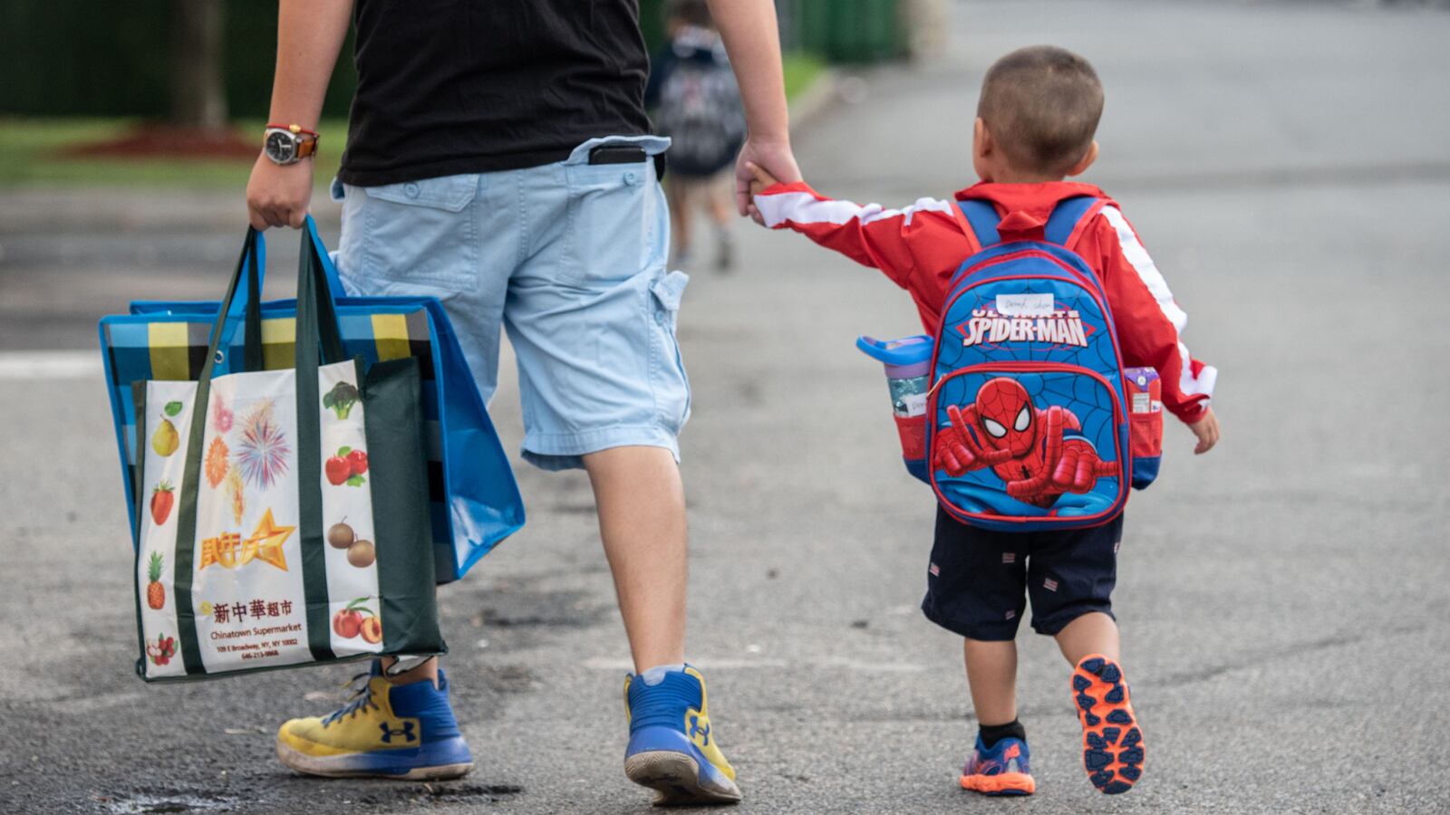 A father holds his child’s hand while walking in the street.