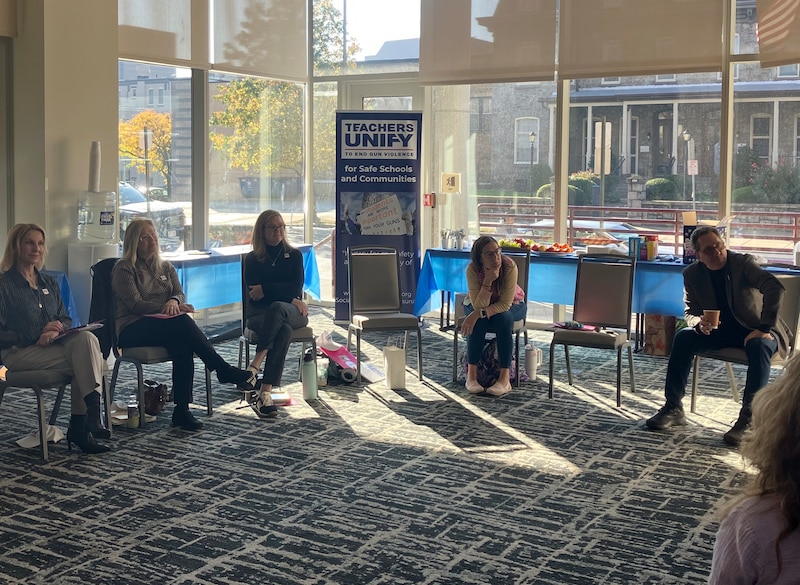 A photograph of a group of people sitting in chairs in a circle in a hotel conference room.