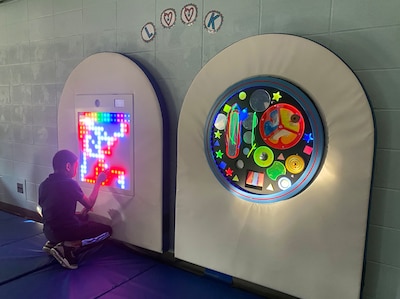 A young student kneels down in front of an interactive art in a room.