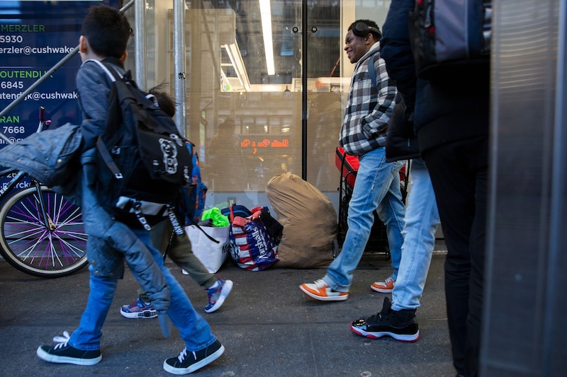 Two young students walk past a couple of adults with a door in the background.