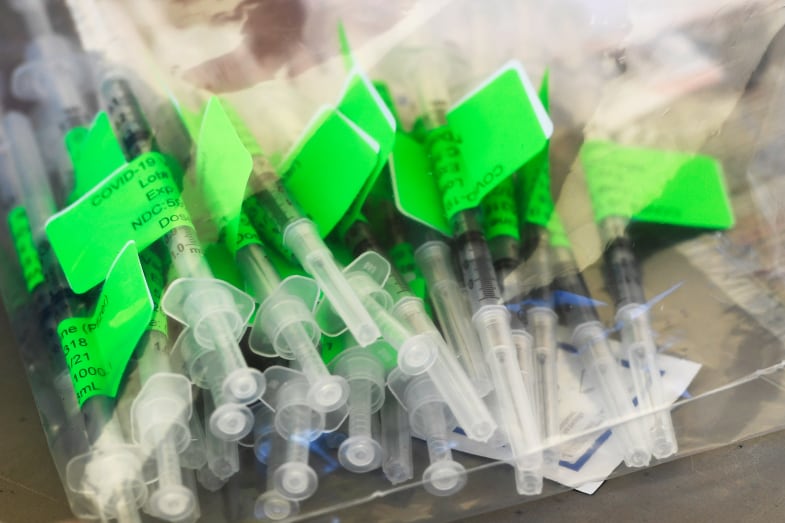 A pile of COVID-19 vaccine syringes with green labels