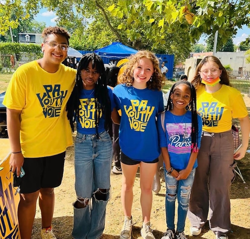 Five high school students stand in a row posing for a photograph outside on a sunny day.