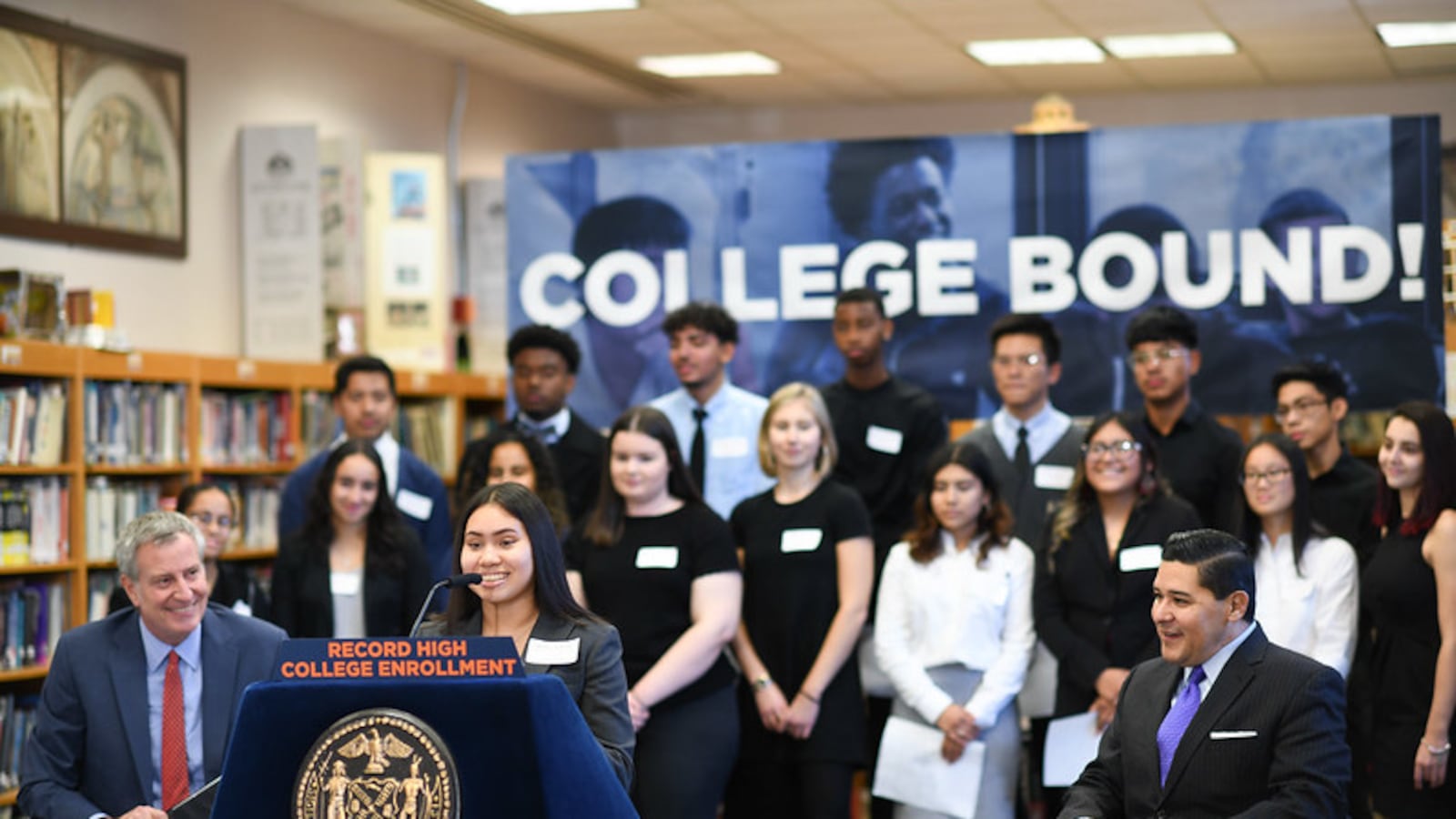 At a press conference about college enrollment, Mayor Bill de Blasio and Chancellor Richard Carranza listen to an alum of High School of Telecommunication Arts and Technology talk about her experience enrolling in college.