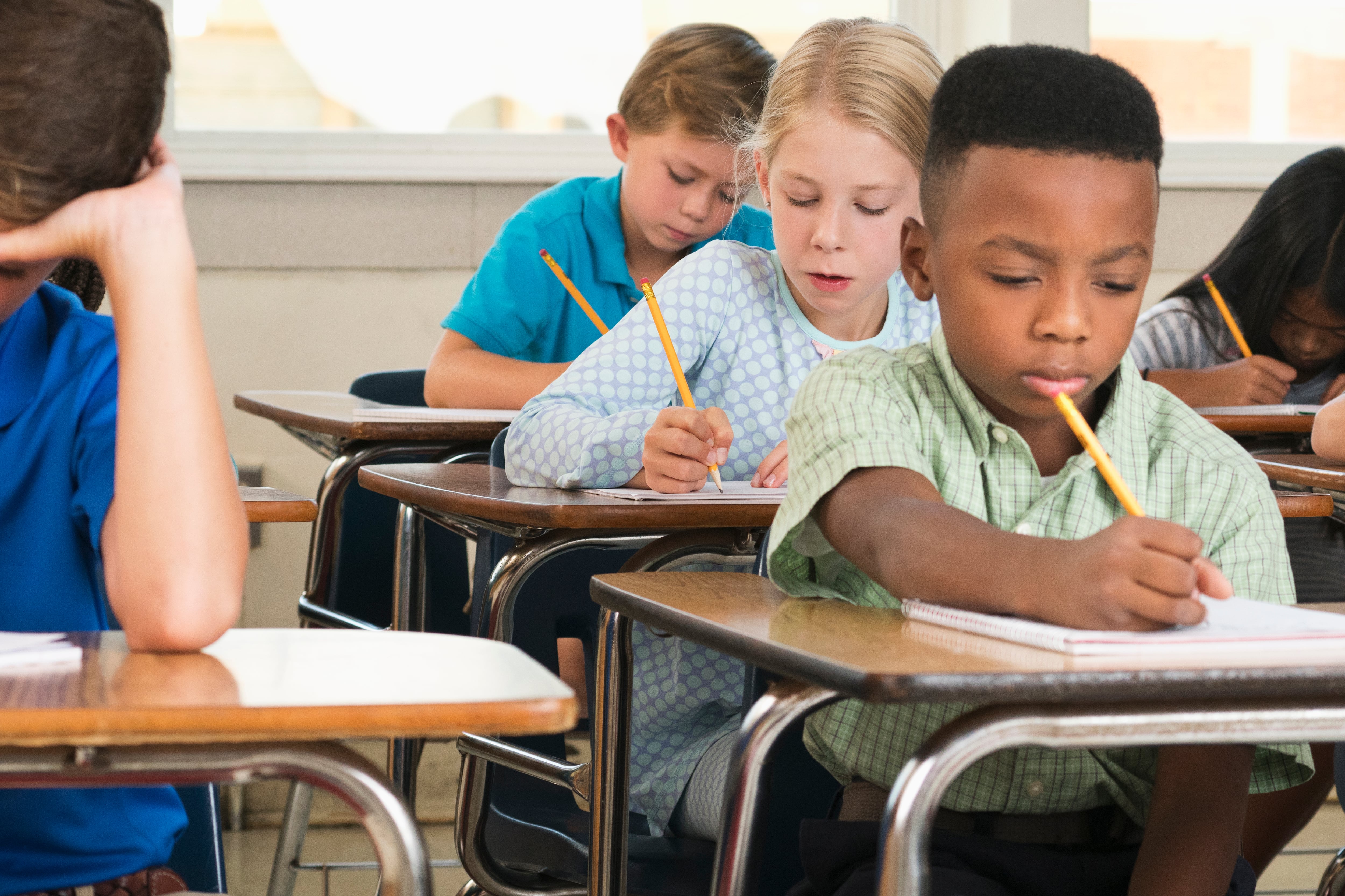Students sit at desks holding pencils.