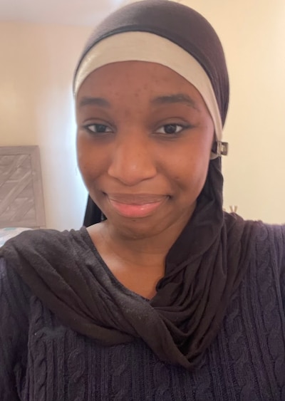 Headshot of a young woman wearing a black top and a black and white head covering.