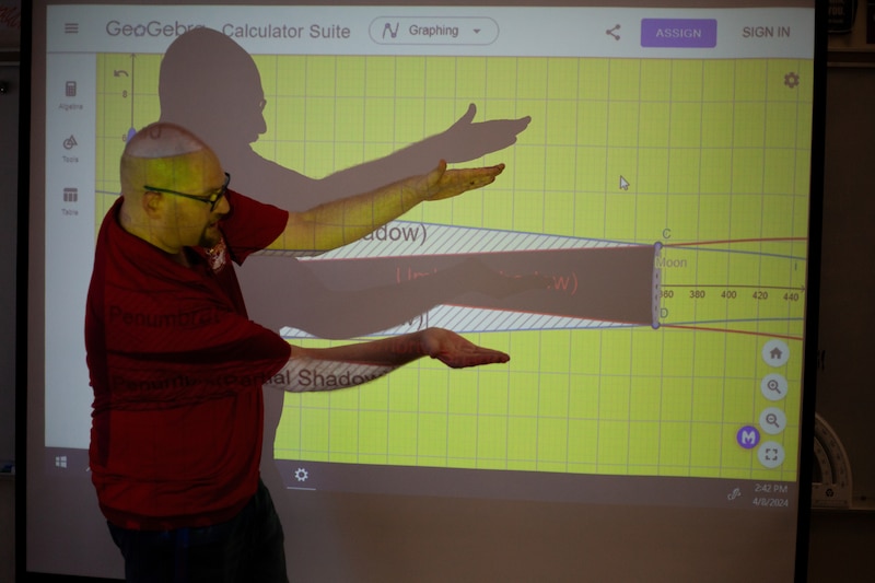 A man wearing a red shirt teaches class at a projector.