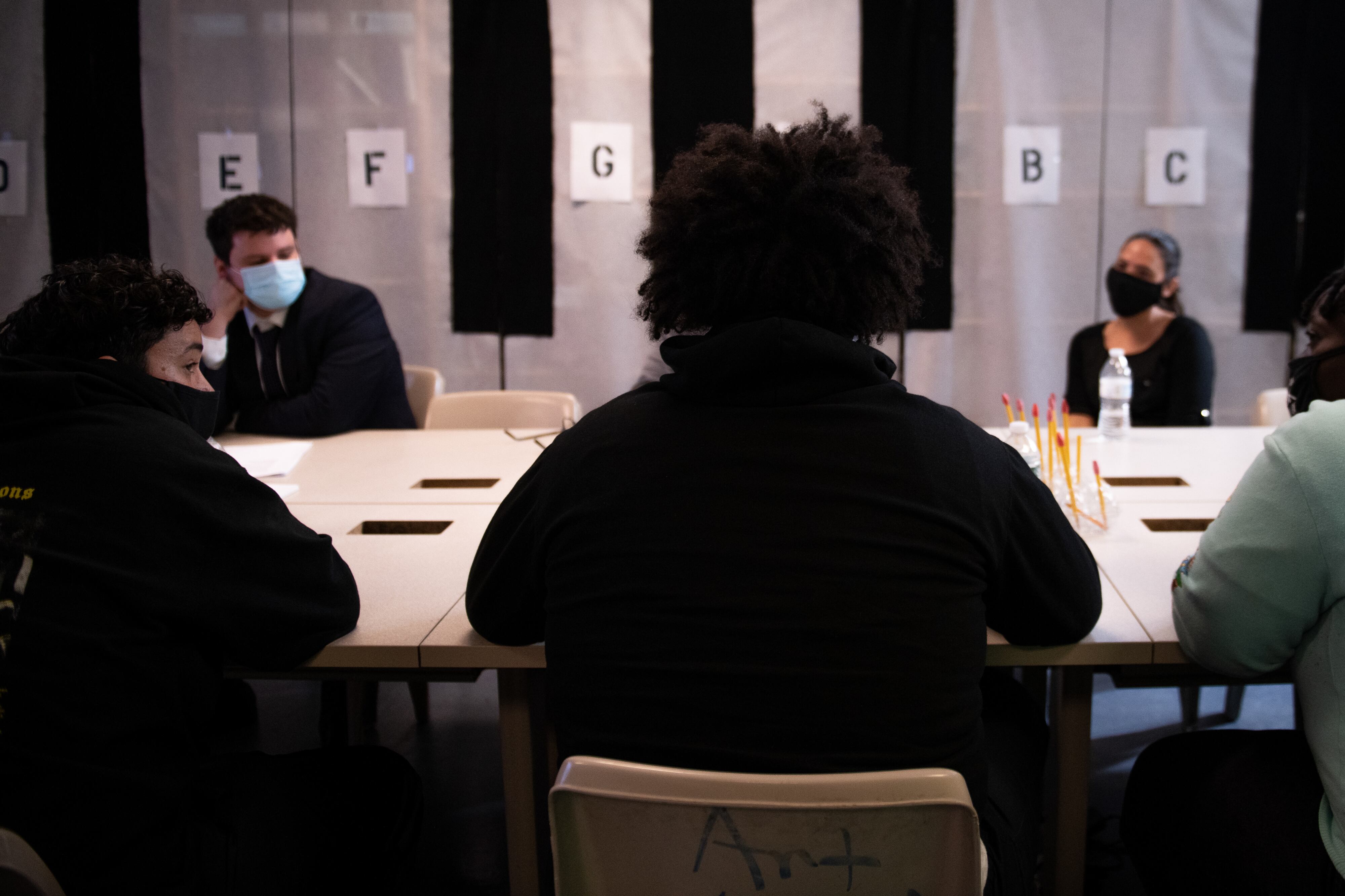 Students and faculty talk around a large conference table, all wearing protective masks.