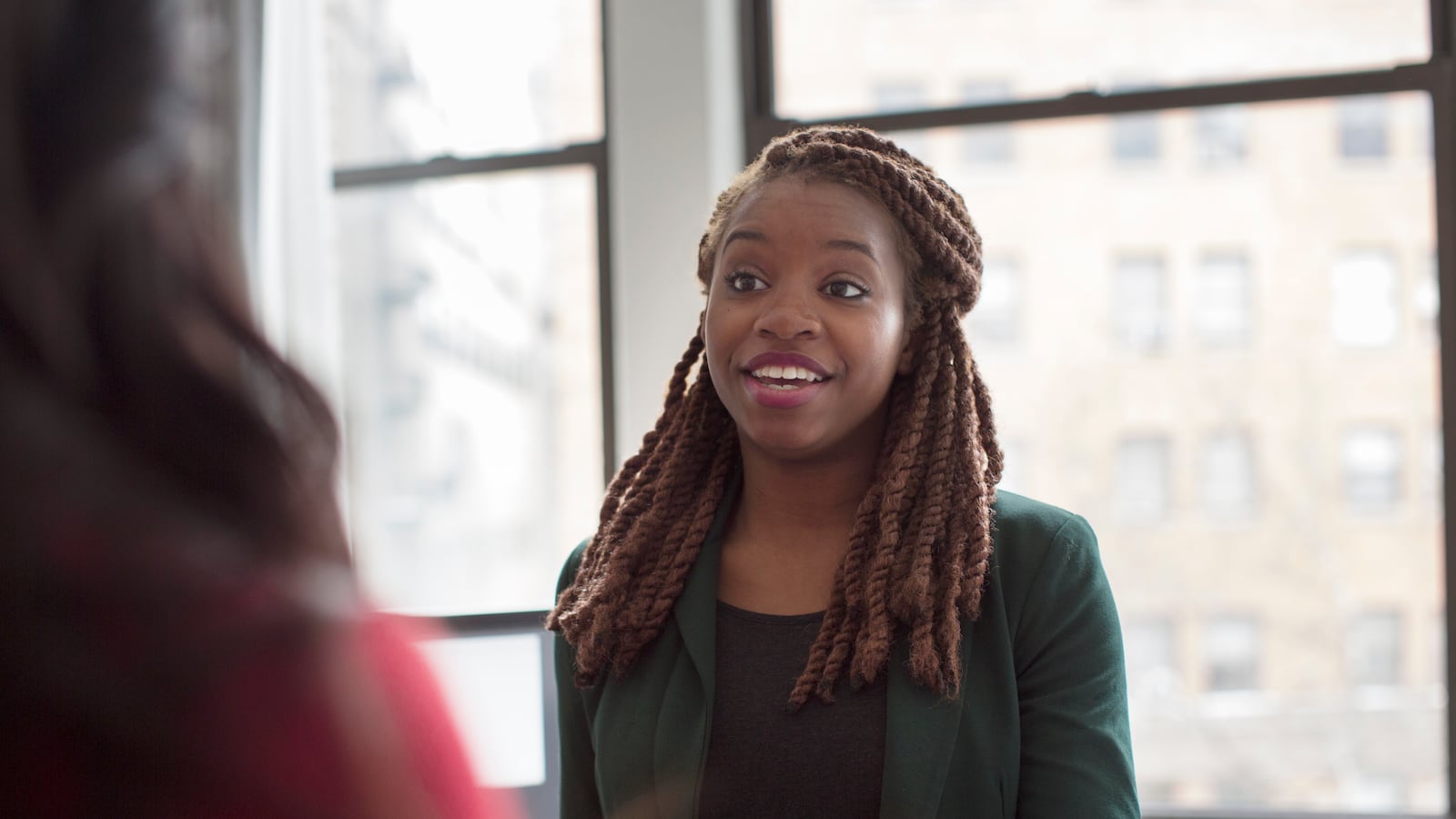 A Black woman wearing a green business suit speaks with a colleague.