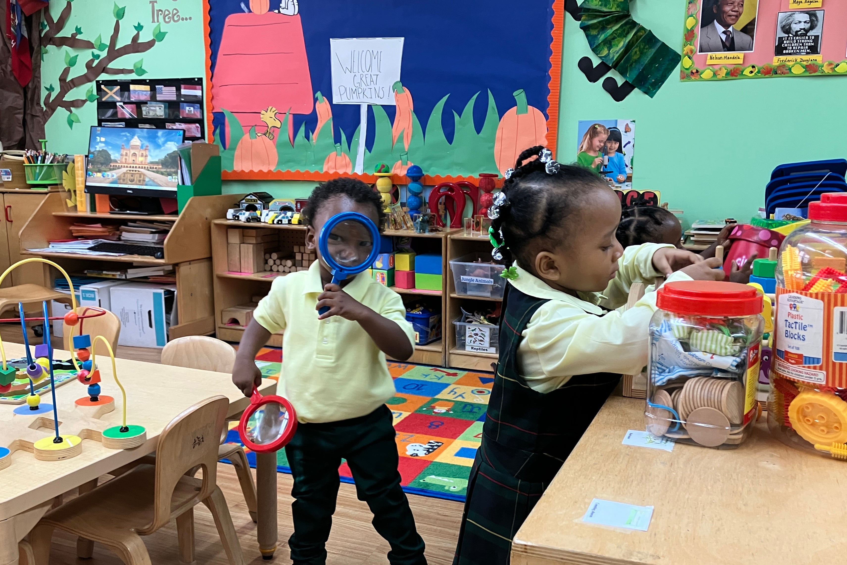 Three young black students play in a colorful classroom.