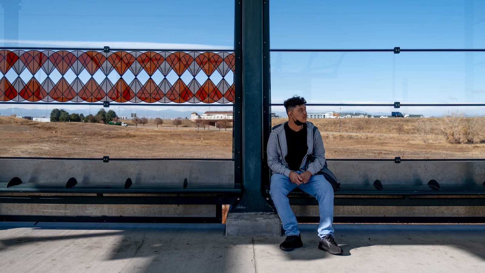 A young man, wearing a grey sweatshirt and blue jeans, waits for his train to arrive to the 40th Avenue station.