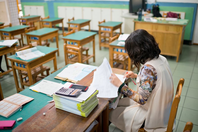 A teacher grades papers in an empty classroom.