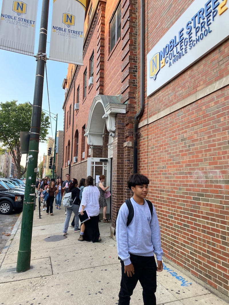 Students walk near the front entrance of a red brick school building.
