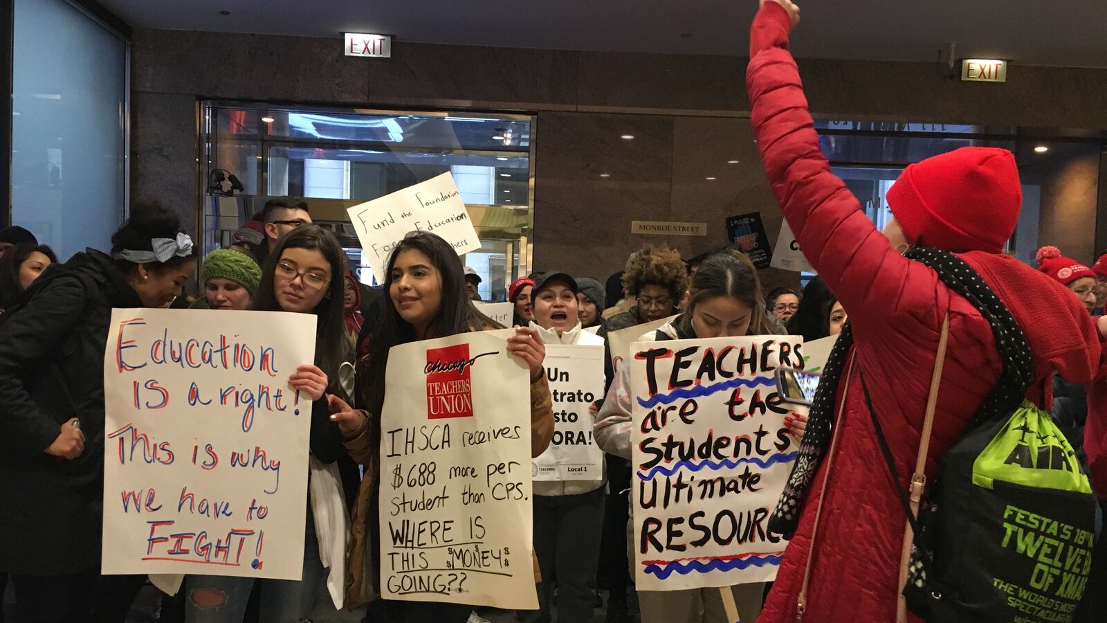 Teachers and students stand in the lobby of a building where their network is holding a board meeting.