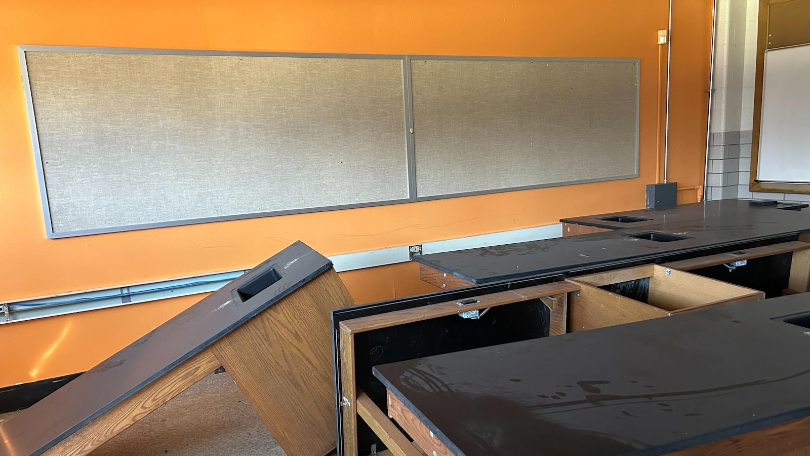 An empty classroom with a bright orange wall in the background.