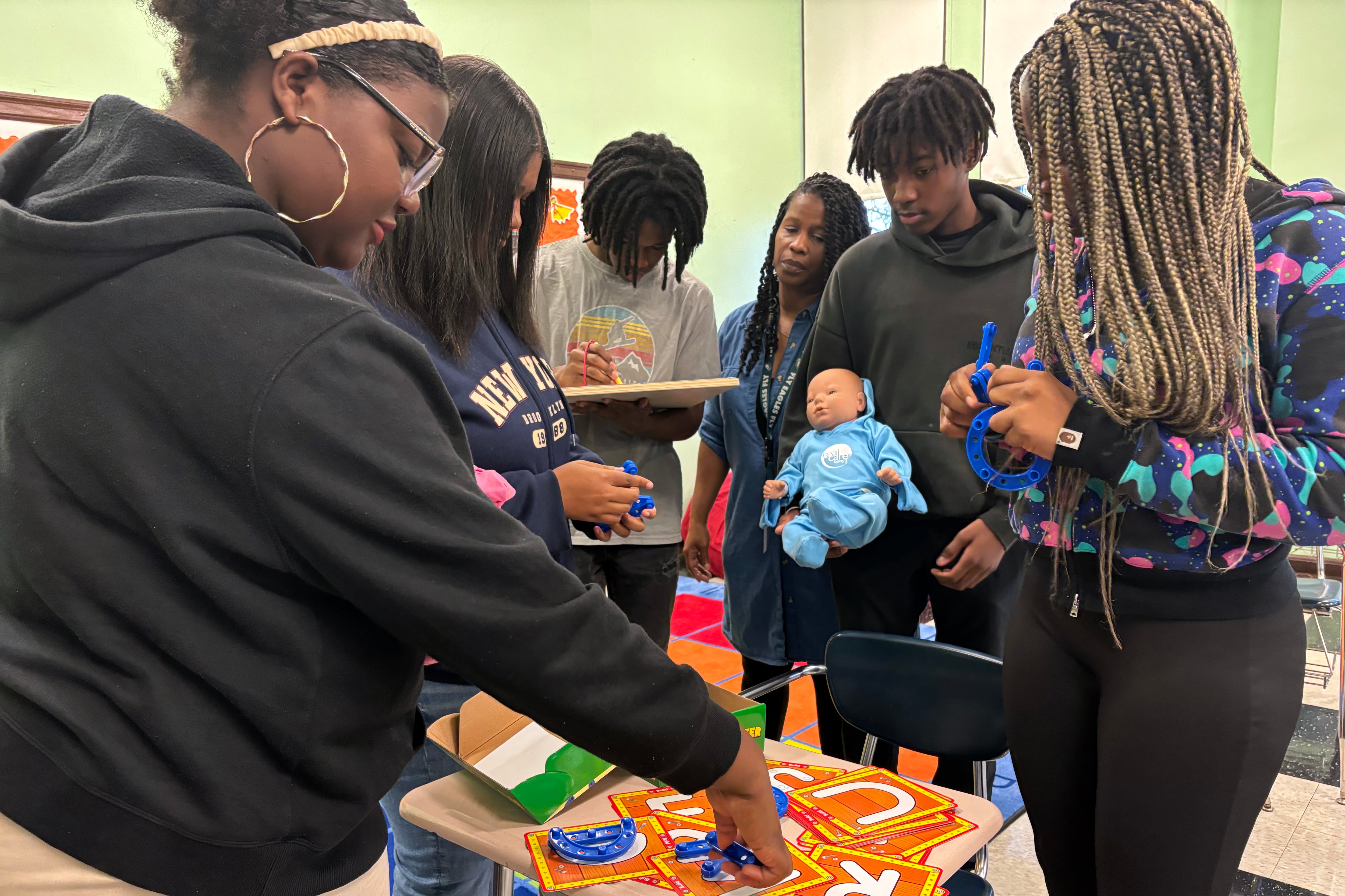 A group of high school students work with dolls in a classroom.