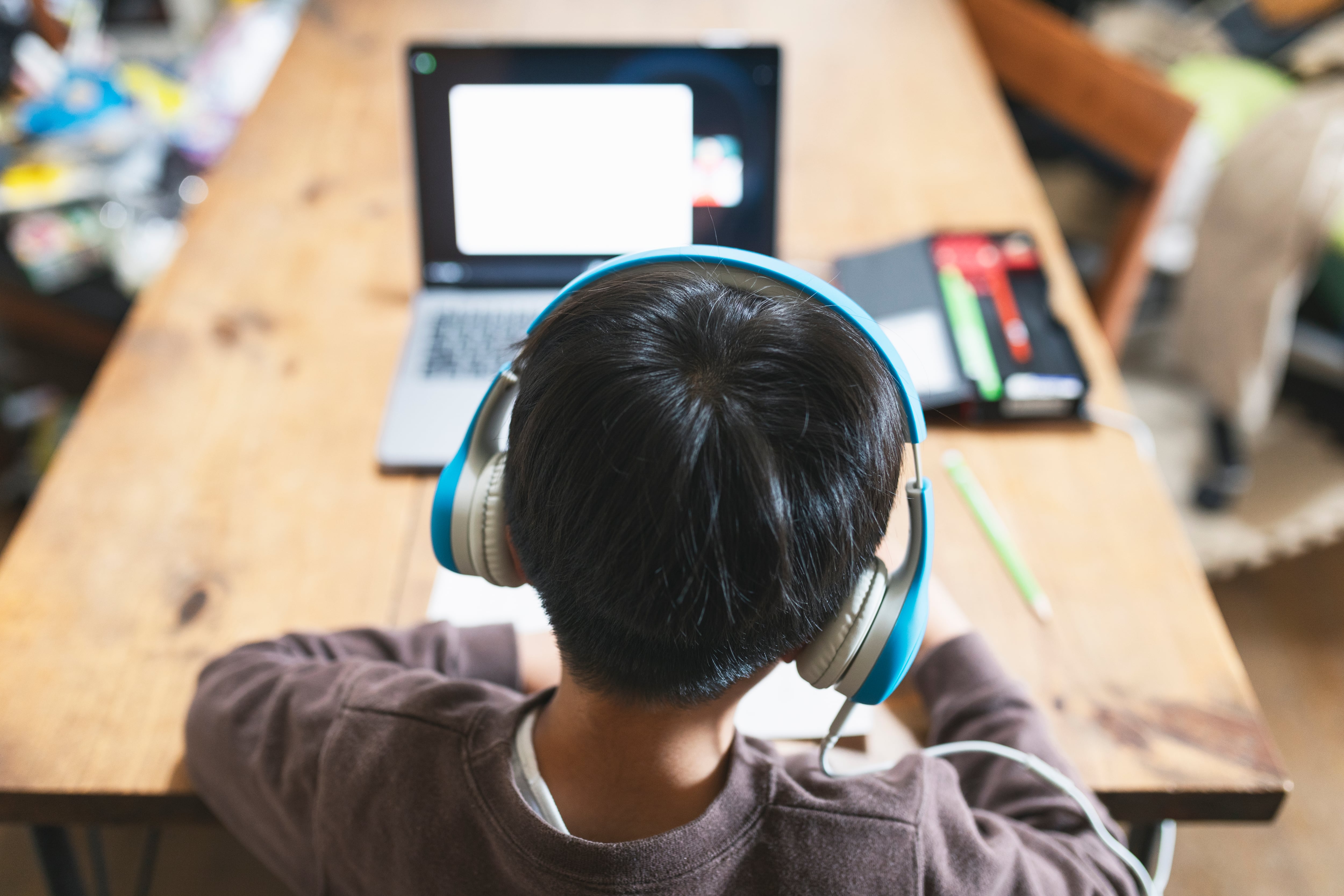 Student wearing headphones sits at a table with a laptop.