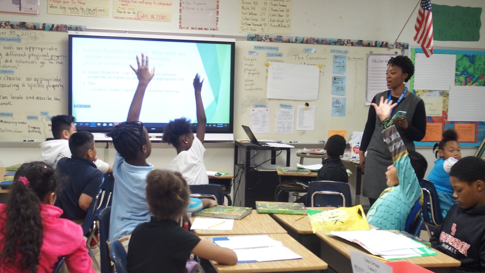 Three students raise their hands to answer a teacher’s question, sitting at their desks in a Memphis classroom.