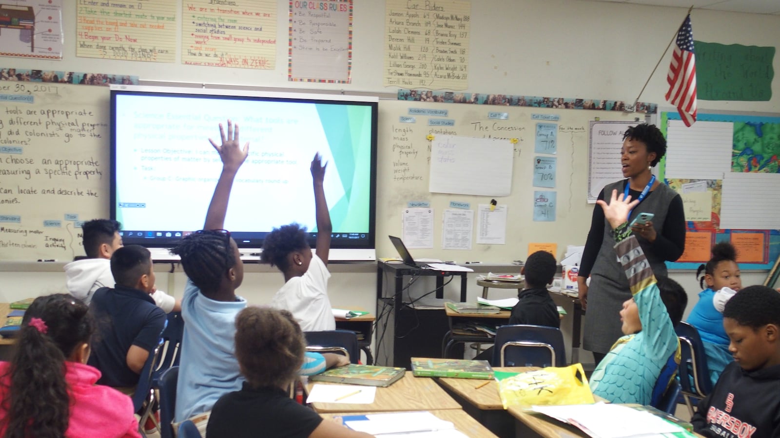 Three students raise their hands to answer a teacher’s question, sitting at their desks in a Memphis classroom.