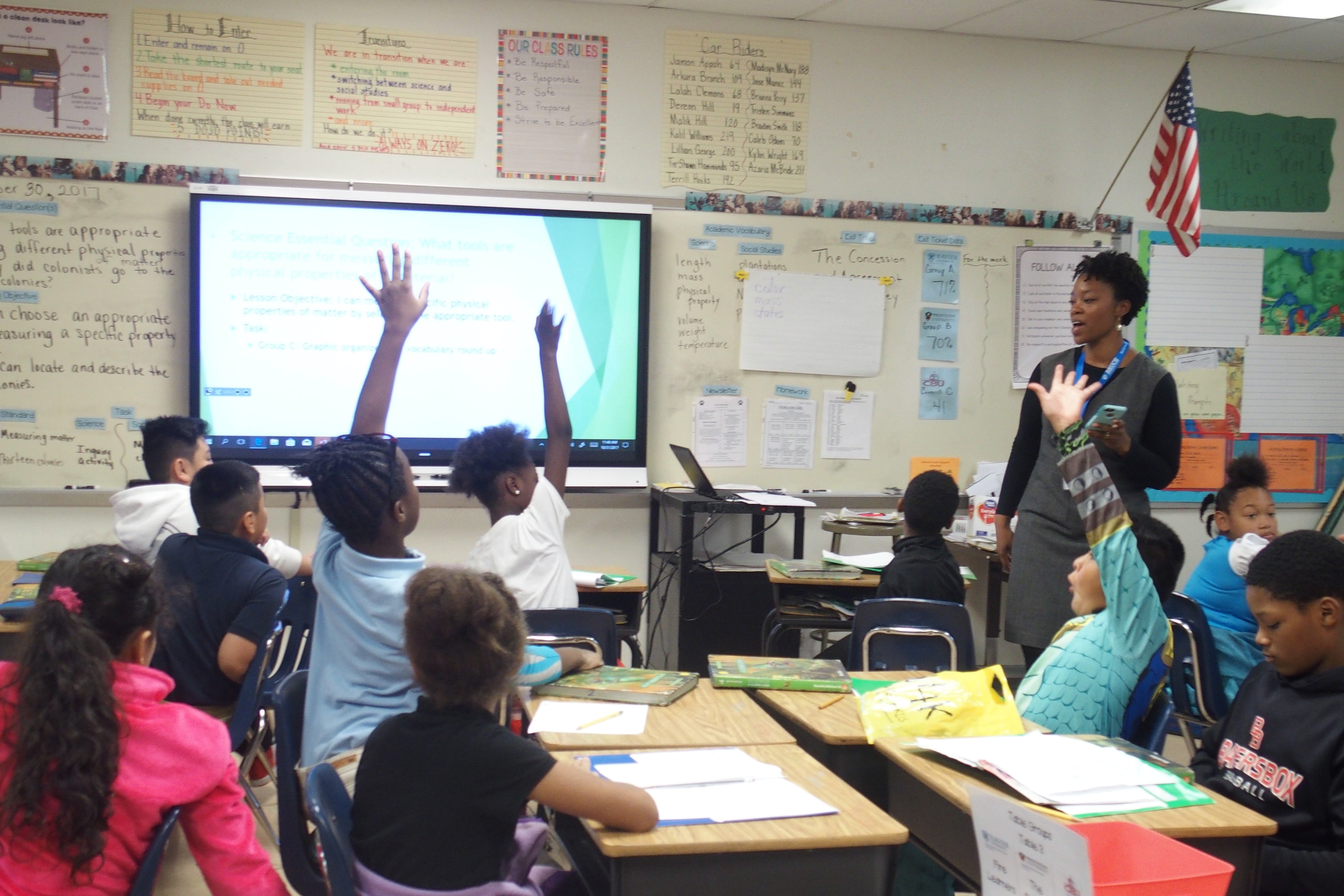 Three students raise their hands to answer a teacher’s question, sitting at their desks in a Memphis classroom.