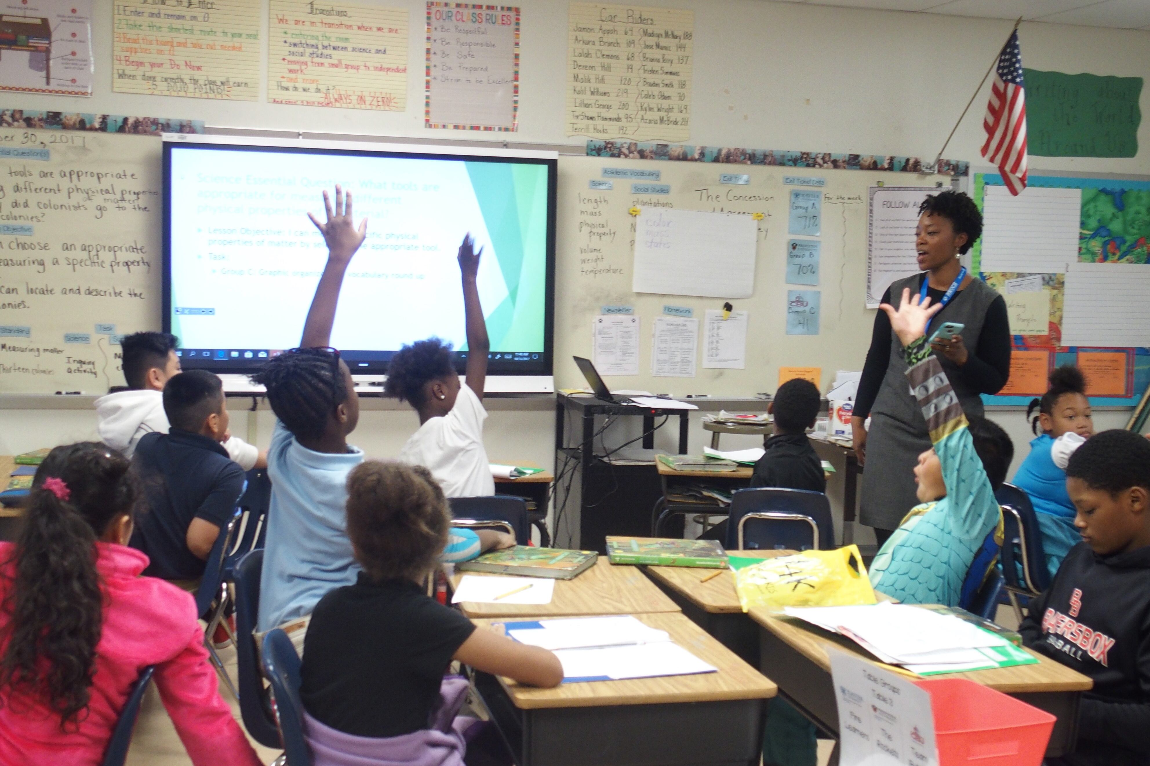 Three students raise their hands to answer a teacher’s question, sitting at their desks in a Memphis classroom.