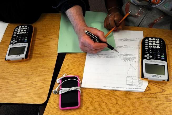 A students with a pencil writes on a white piece of paper with calculators and a green piece of paper nearby.