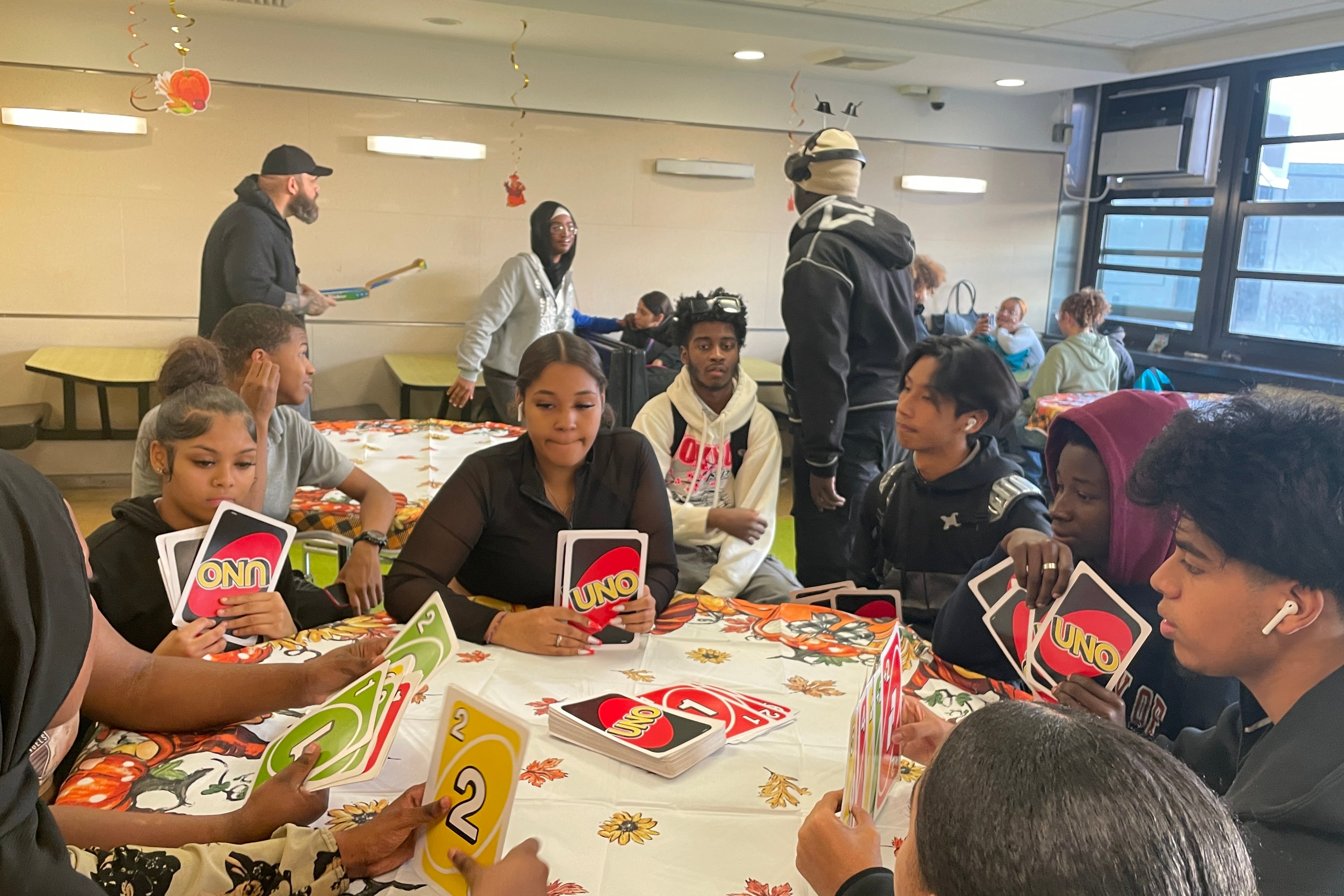 A group of students sit at a table playing Uno with large format cards.