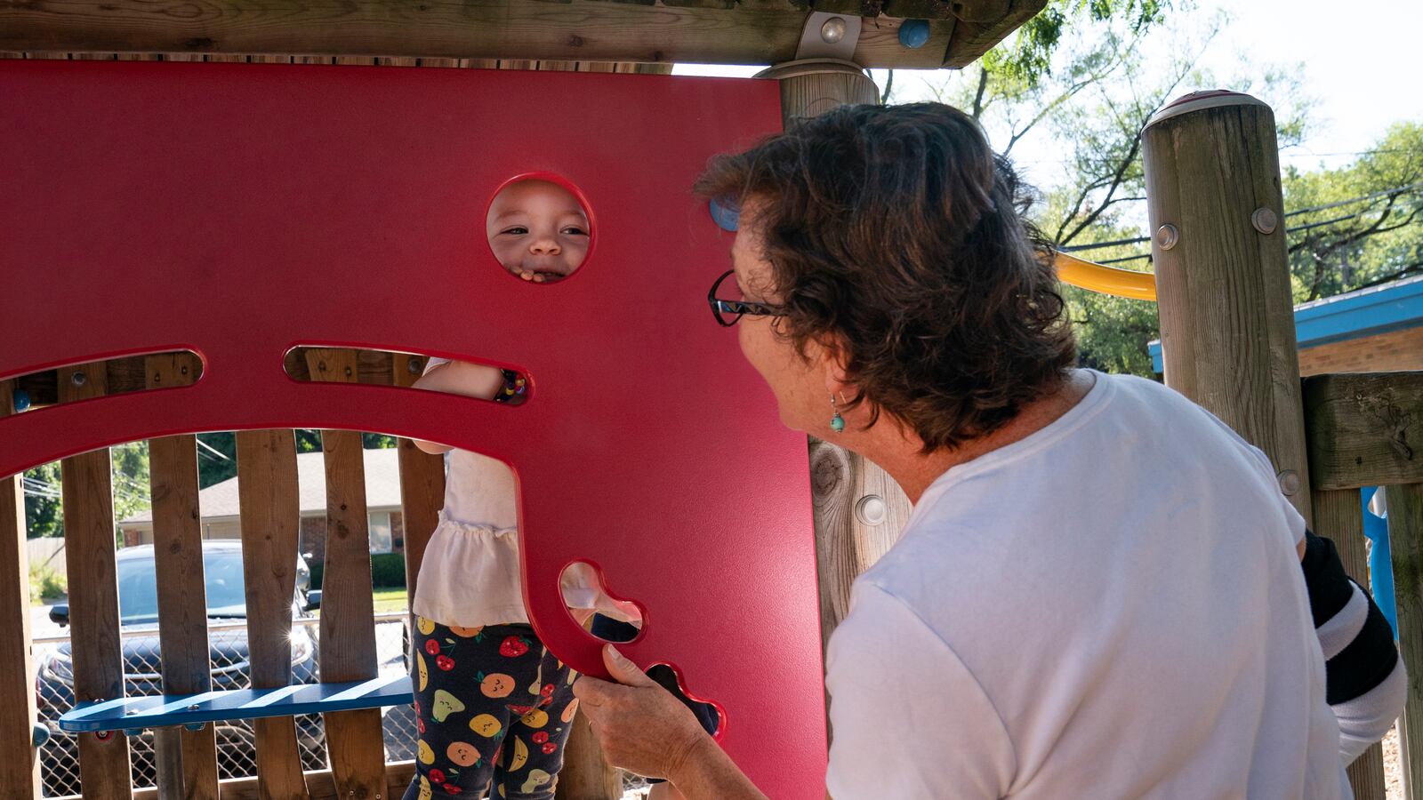 A little boy is playing in a outdoor play structure at Ferndale Montessori, while the owner of the center looks on.