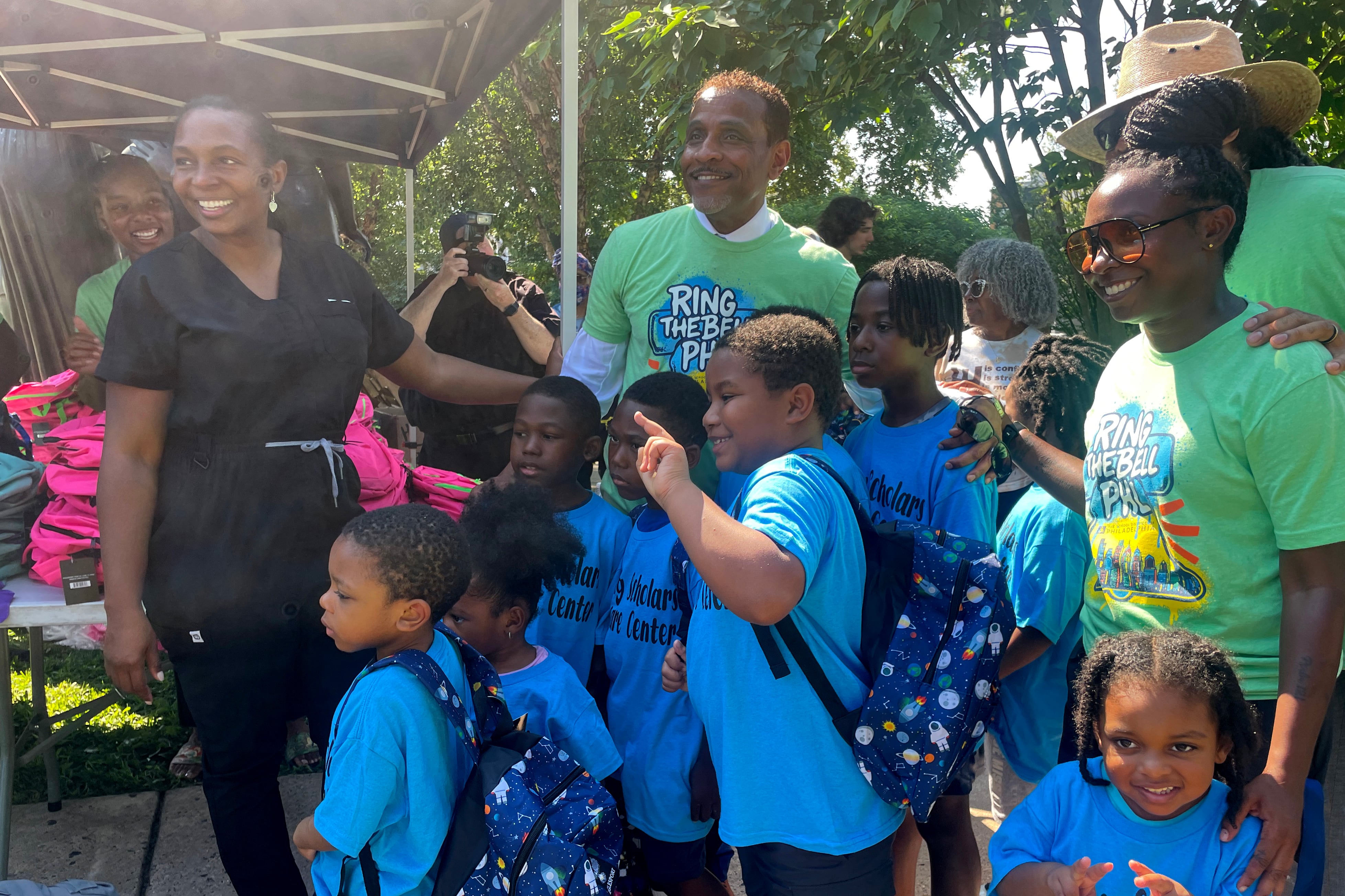 A photograph two adults standing next to a group of young students outside.