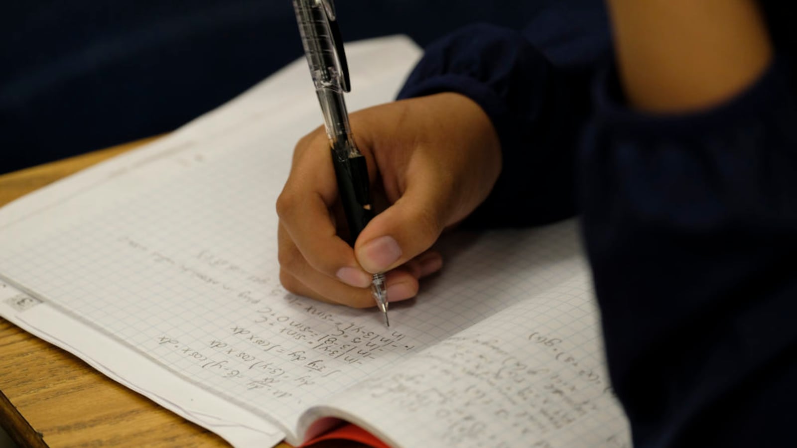A student writes with a pen at his desk in a classroom.
