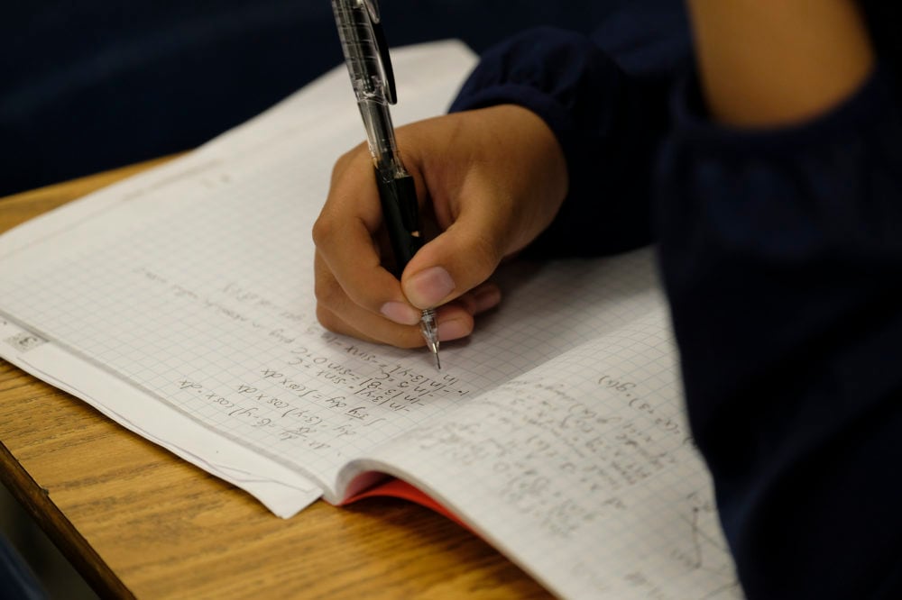A student writes with a pen at his desk in a classroom.