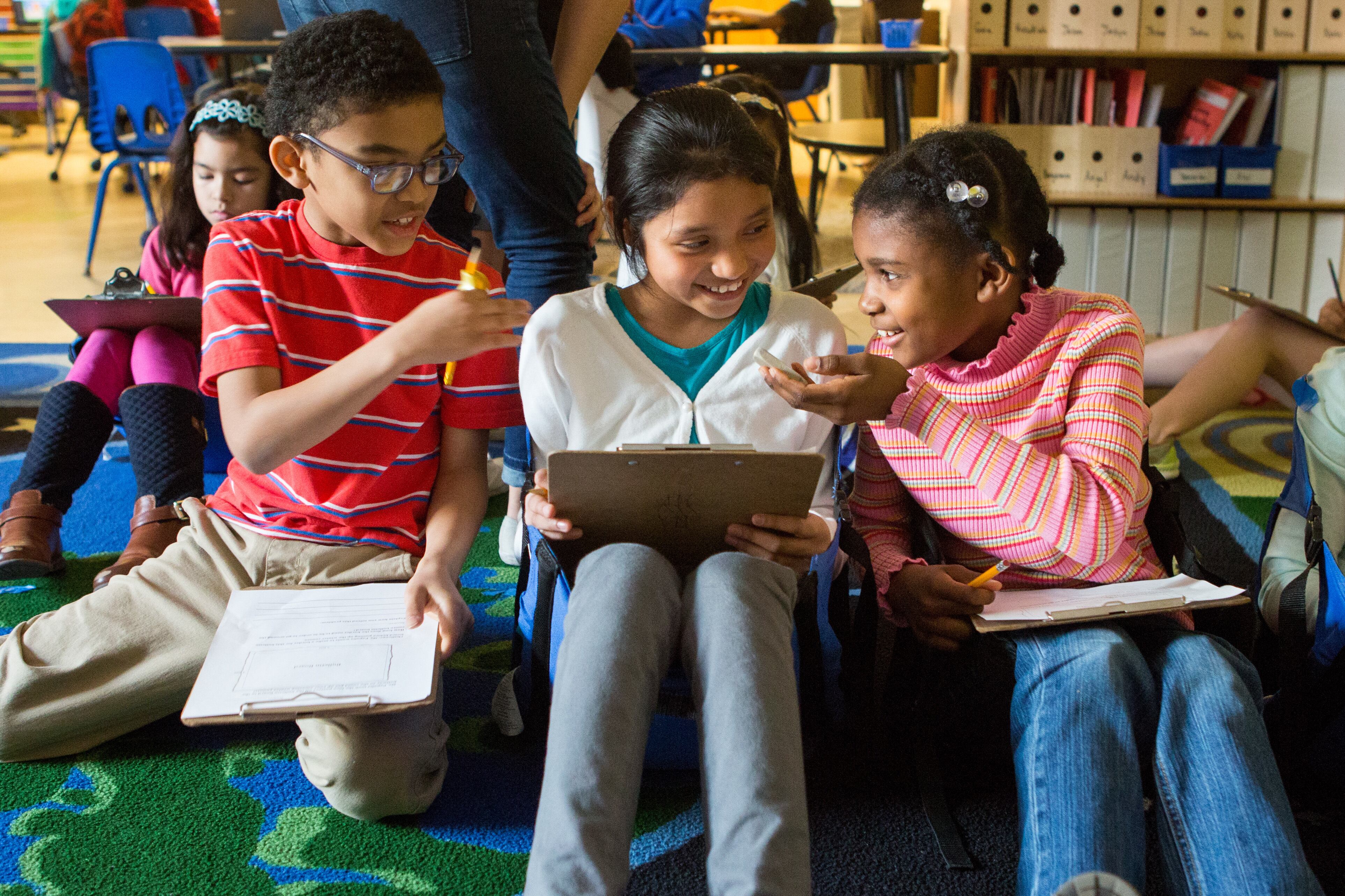 Three young students sit on their floor in their classroom working on a math problem.