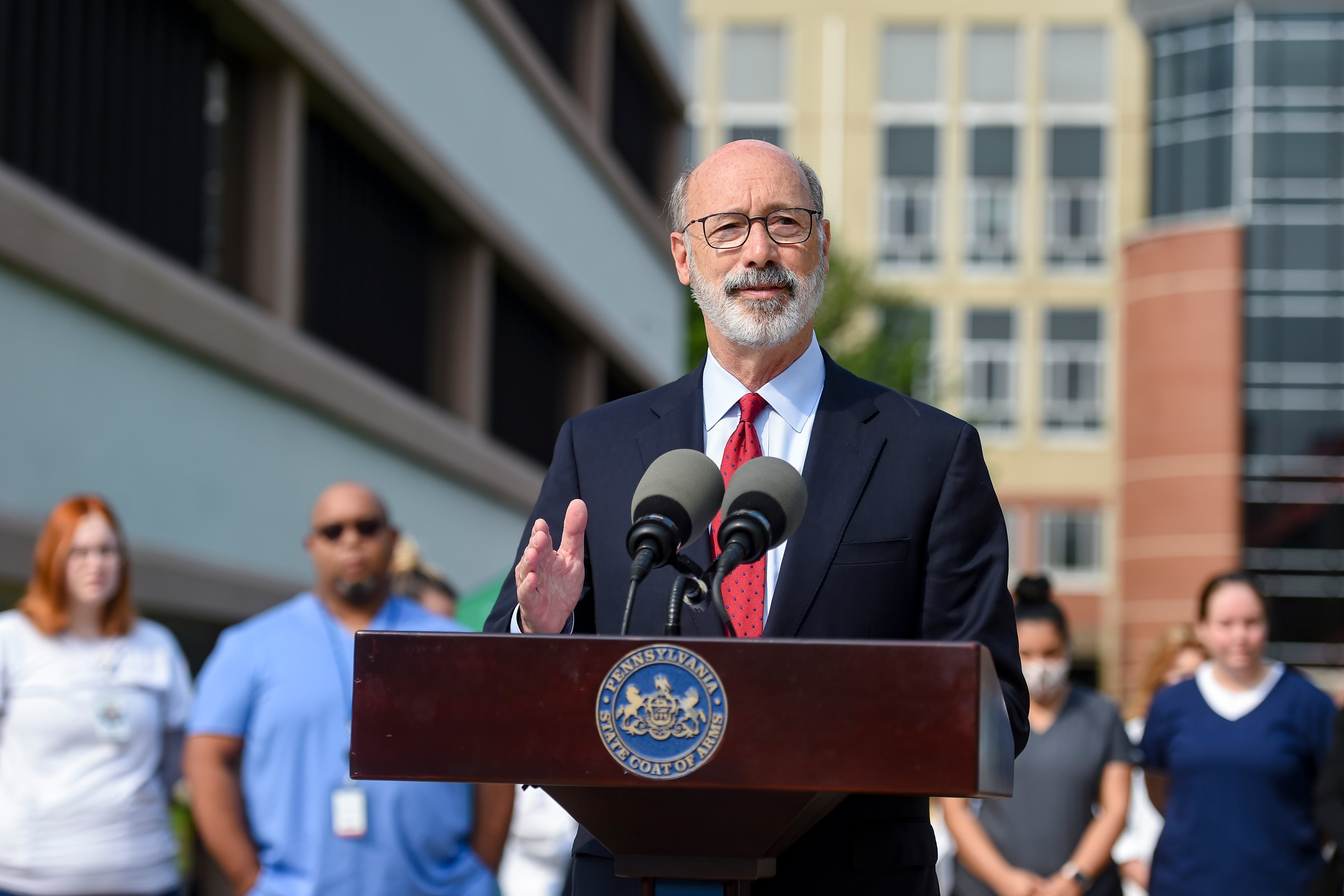 Pennsylvania Governor Tom Wolf speaks at a podium as people stand behind him.