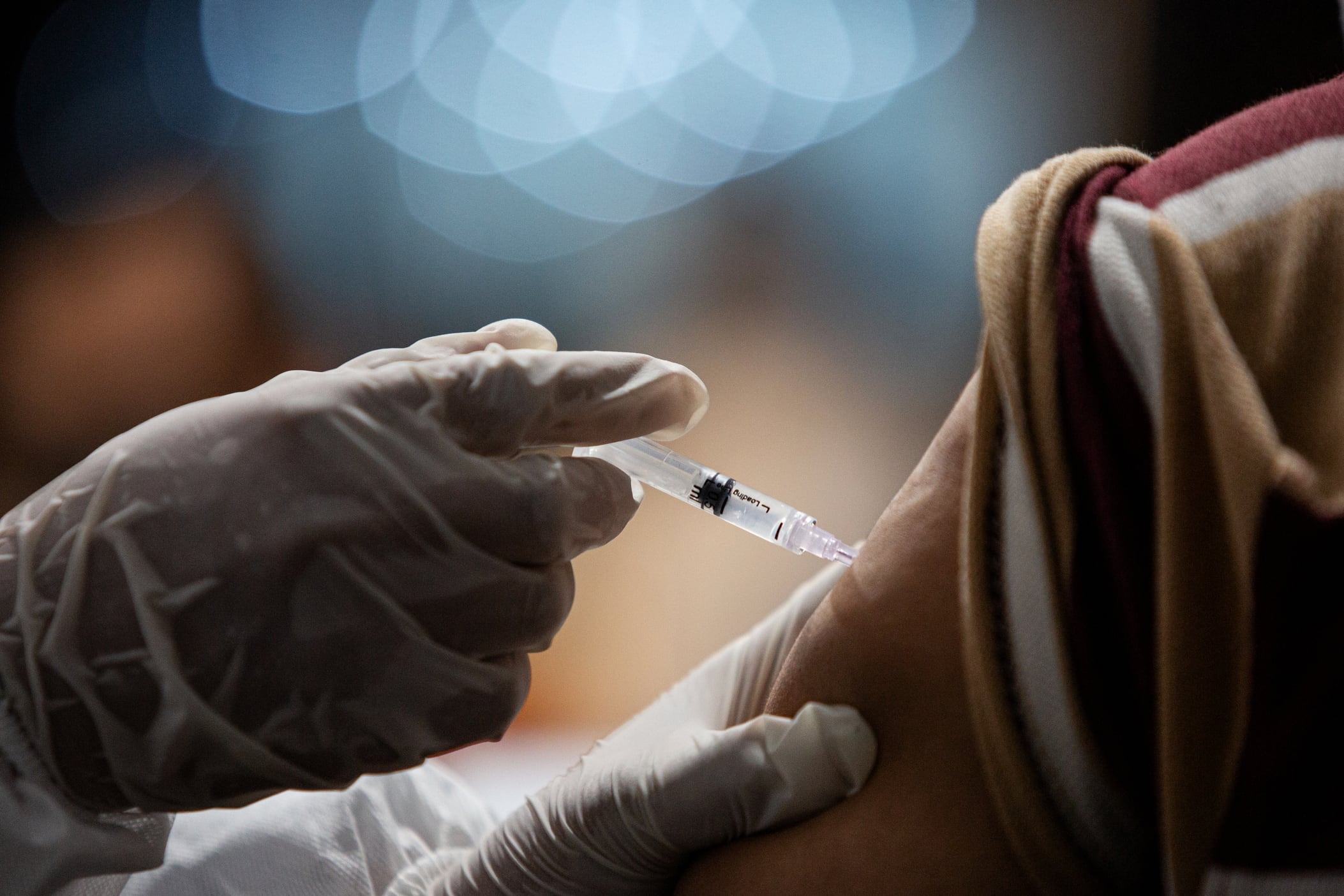 A health care professional wearing latex gloves injects a dose of the COVID vaccine into a person’s arm.
