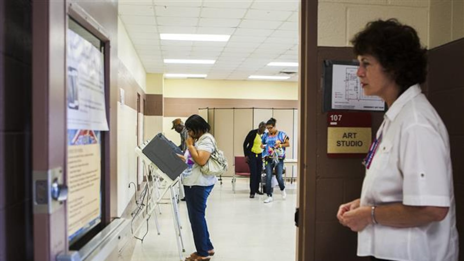 Linda-Marie Goetze (right), officer, Shelby County Election Commission, waits patiently outside a doorway of an early voting precinct, Dave Wells Community Center, for voters as Mary Wilkins (second from left) ponders a decision at a voting booth in North Memphis.