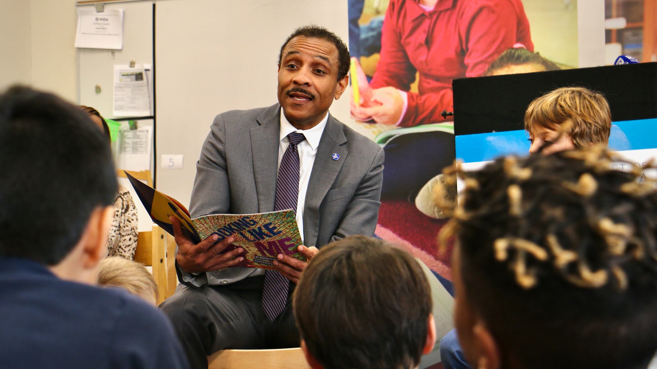 A man in a gray suit reads a book to young children
