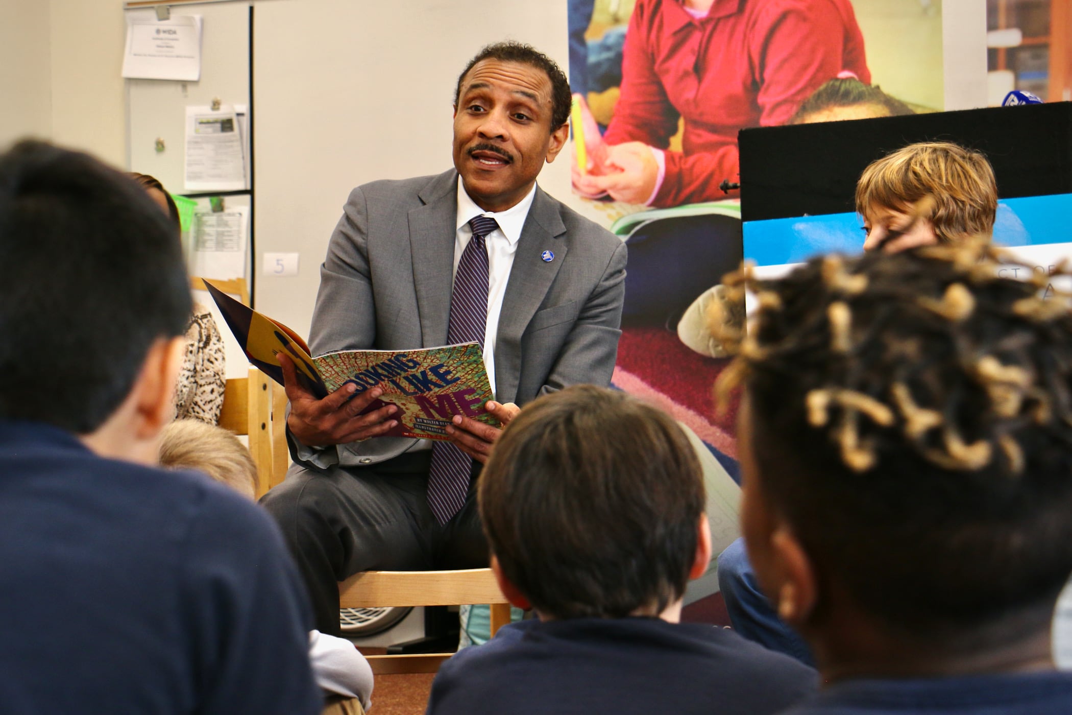A man in a gray suit reads a book to young children