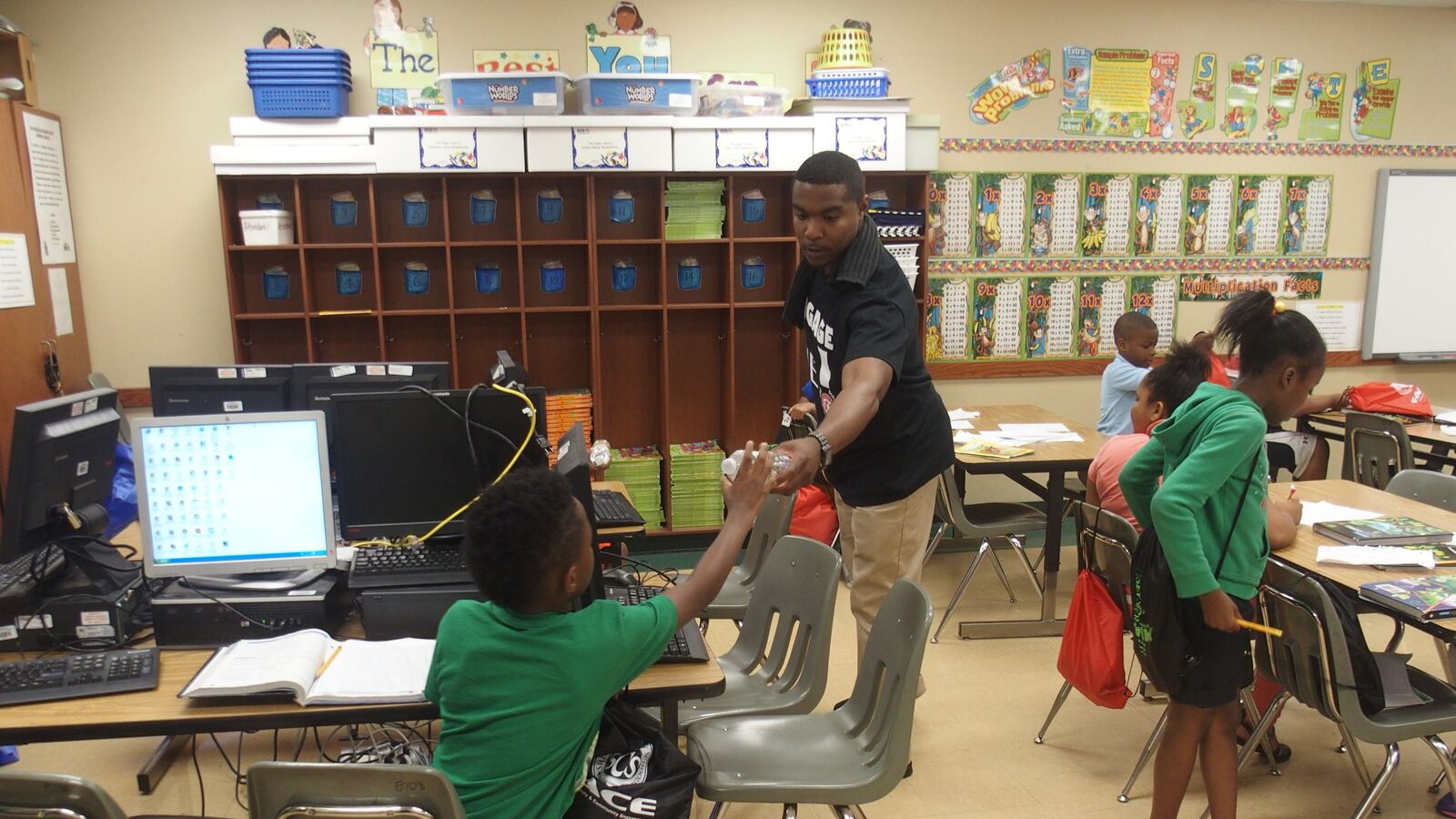 An engagement team member for Shelby County Schools hands out packets filled with reading books and district paraphernalia to children during a summer school program at Winridge Elementary School in Memphis.