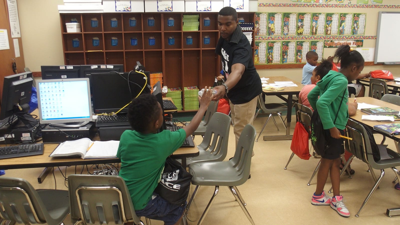 An engagement team member for Shelby County Schools hands out packets filled with reading books and district paraphernalia to children during a summer school program at Winridge Elementary School in Memphis.