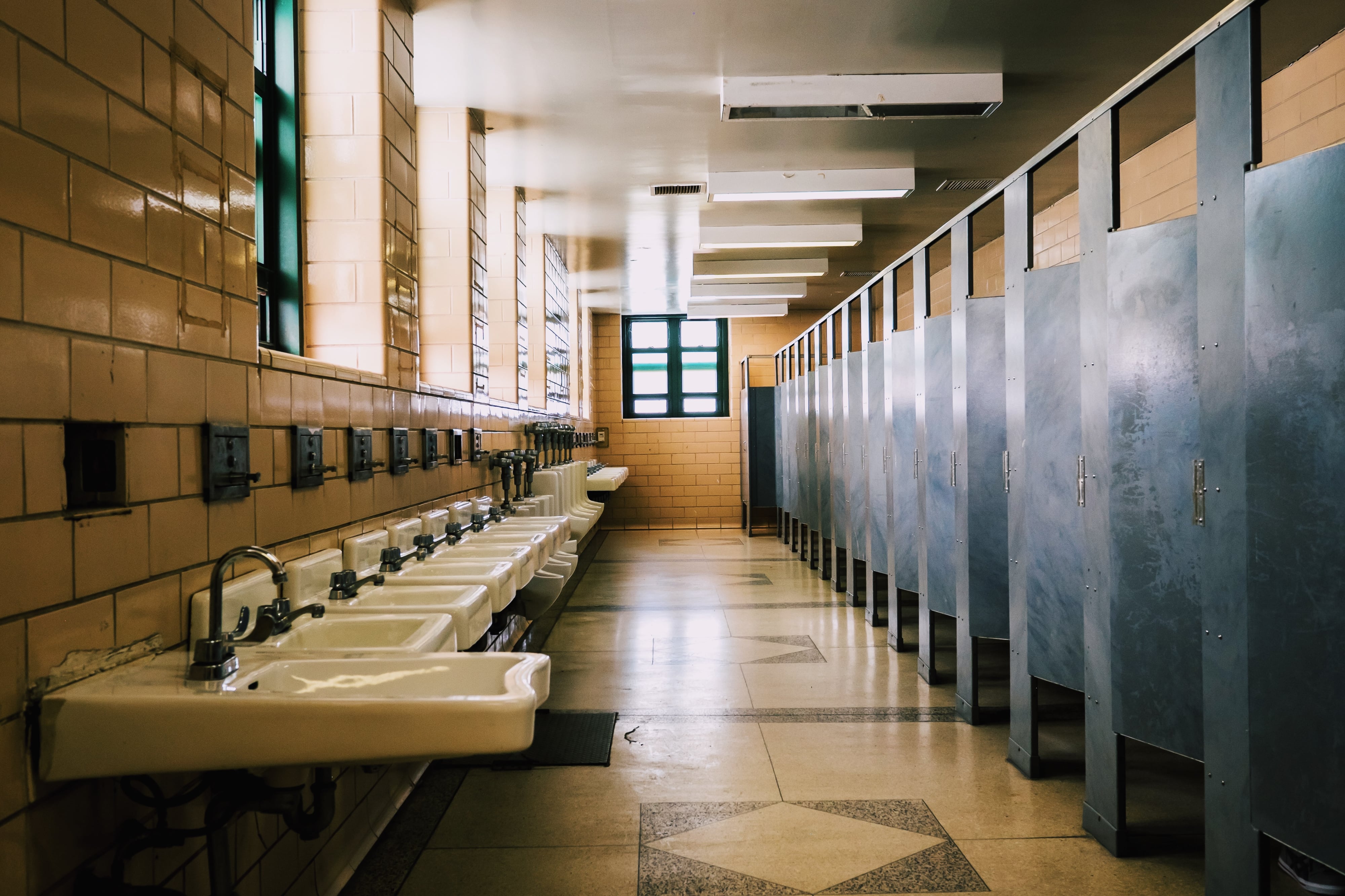 A public bathroom with blue stalls, a long row of sinks and tiled walls and floors.