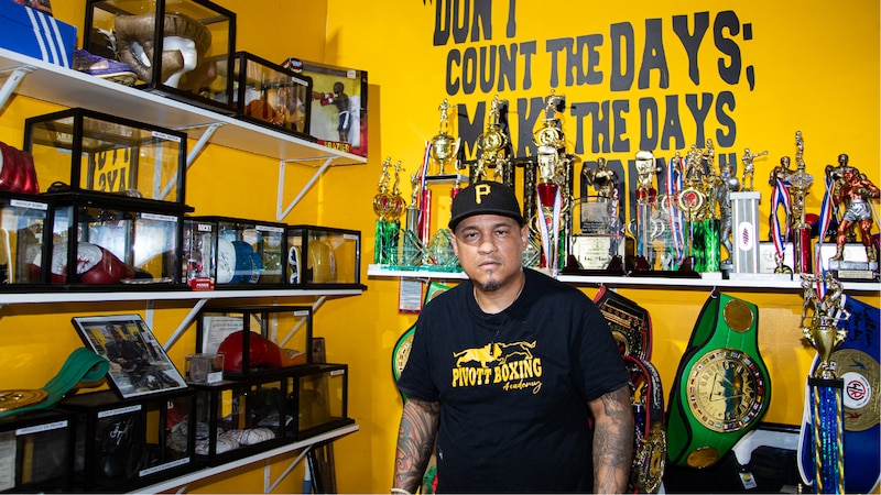 A photograph of a man posing for a portrait with trophies in the background.