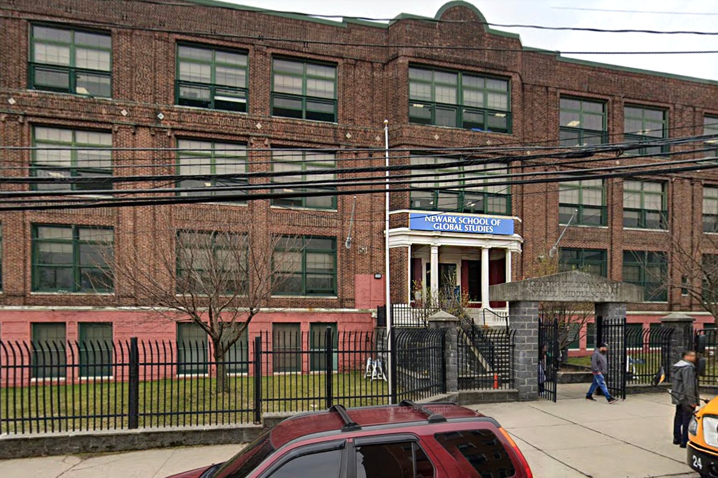 A brick building is seen behind a small black fence.
