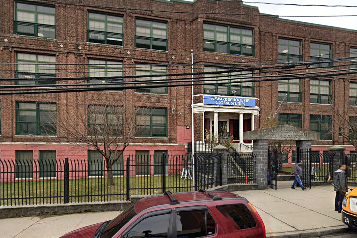A brick building is seen behind a small black fence.